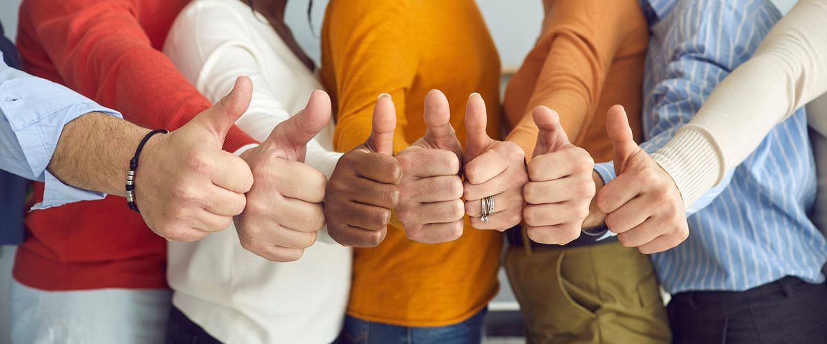 Mehrere Personen zeigen gemeinsam den Daumen nach oben als Zeichen für Zustimmung und Teamgeist