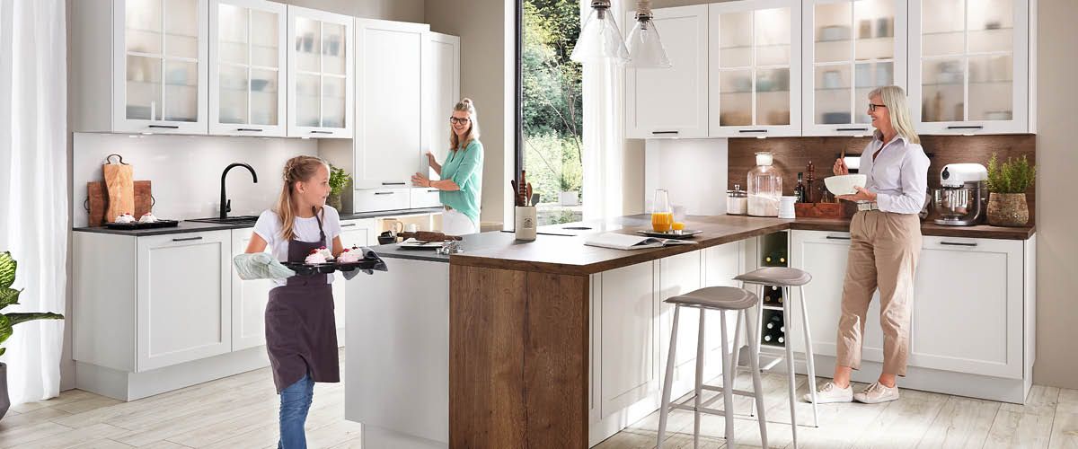 Moderne weiße Wohnküche mit Kochinsel und drei Personen beim gemeinsamen Kochen