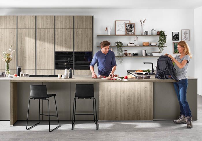 Moderne Holzoptik-Küche mit Kochinsel, offenen Regalen und zwei Personen im Alltag