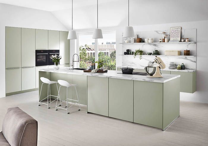 Moderne offene Küche in sanftem Grün mit Kochinsel, Hockern und weißen Hängelampen