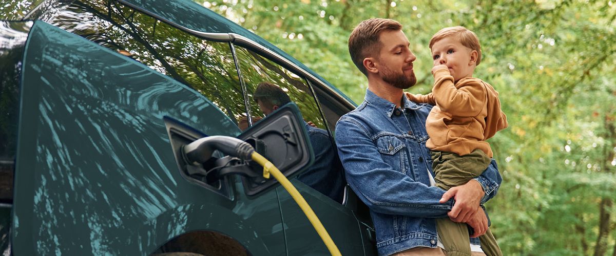 E-Auto laden und Zeit mit der Familie genießen Vater mit Kind neben ladendem E-Auto an einer Ladesäule im Grünen