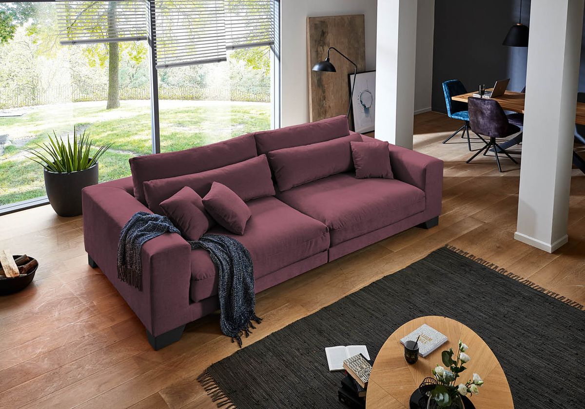 Modernes Wohnzimmer mit violettem Sofa vor großer Fensterfront und gemütlicher Einrichtung. Wohnzimmer